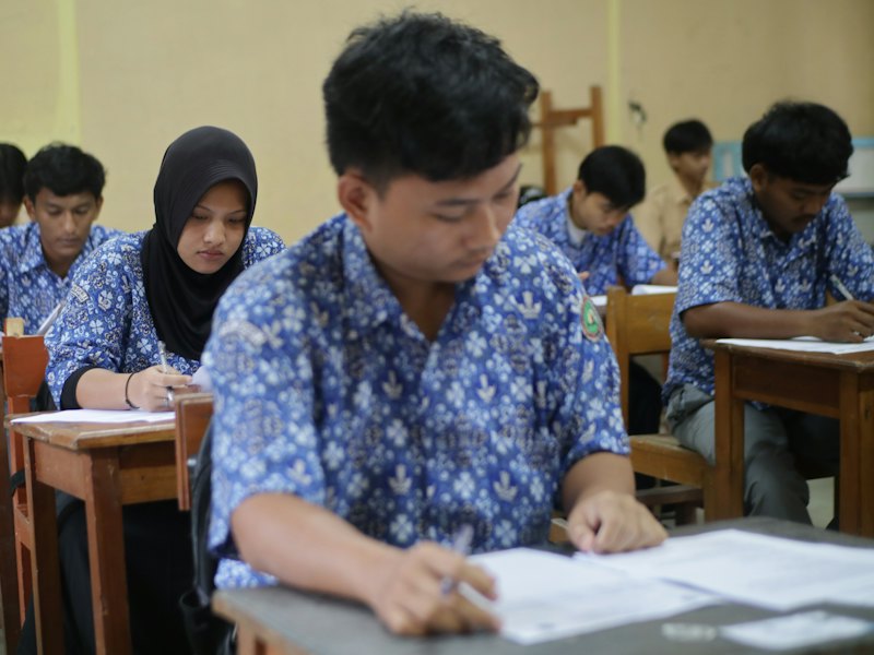 Students in batik uniforms sitting an exam in a classroom