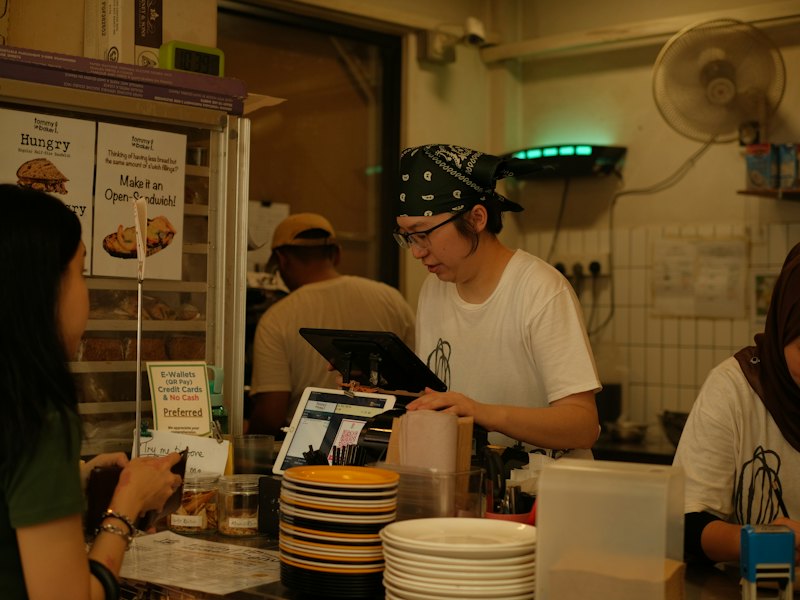 Staff serving customers at a busy food counter with a POS screen